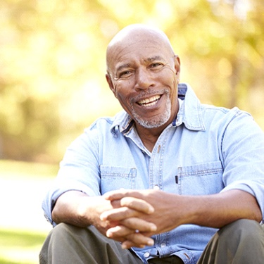 Older man with dental implants in Guilderland smiling outside