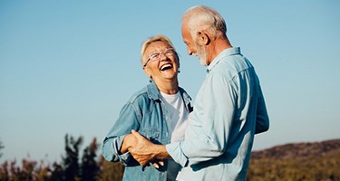 a mature couple smiling from the benefits of dentures