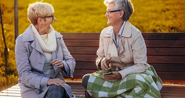 two mature women conversing on a bench outside