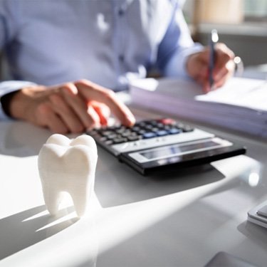 person typing on a calculator next to a false tooth 