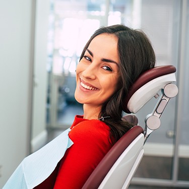 Woman in red shirt sitting in dental chair smiling