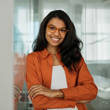 Woman with glasses and orange jacket smiling with arms folded