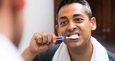 man brushing his teeth in front of his bathroom mirror 