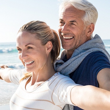 Senior couple with implant dentures in Guilderland, NY smiling on beach