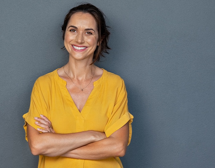 Woman in yellow blouse smiling and standing with arms crossed