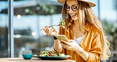 Woman smiling at phone while eating lunch