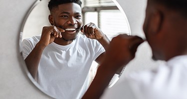 Man smiling while flossing in mirror