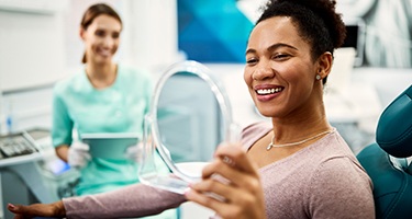 Woman smiling at reflection in handheld mirror