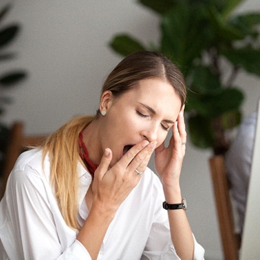 Woman with sleep apnea who needs sleep apnea dentist tired at work