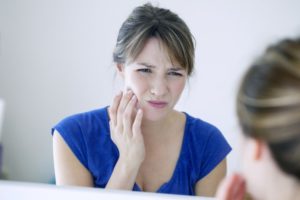 woman with a painful dental emergency holding the side of her jaw 