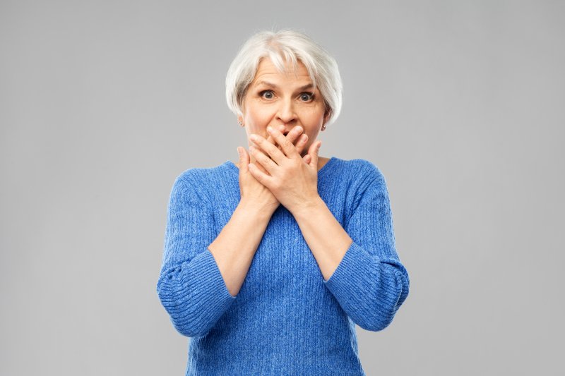 Elderly woman in blue knitted sweater covering mouth with both her hands