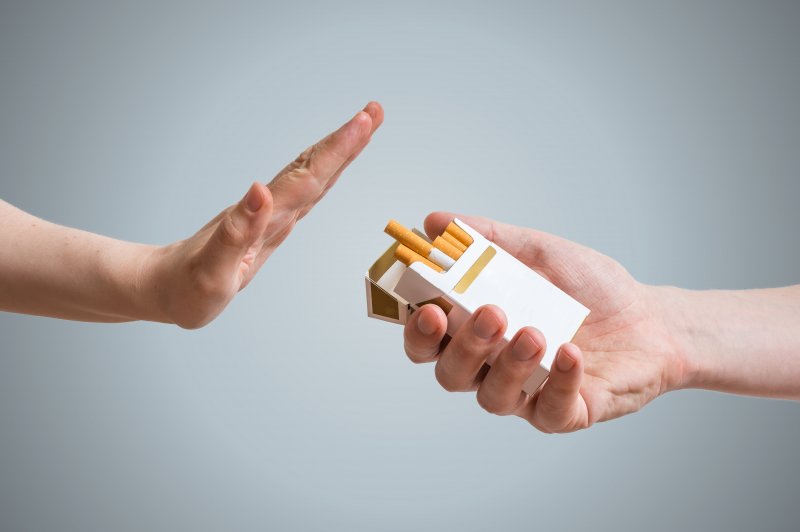 Hand refusing another person's hand holding a box of cigarettes