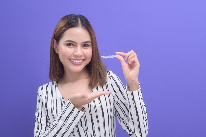 person holding Invisalign and pointing to it while smiling