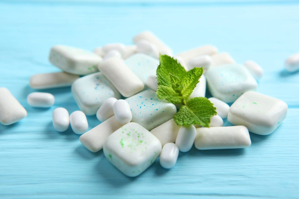 Tic tacs and chewing gum with mint leaf on blue surface