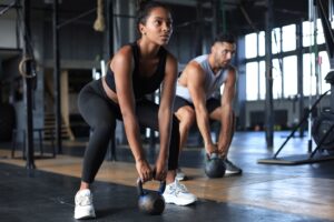 Man and woman squatting holding kettlebells at the gym.